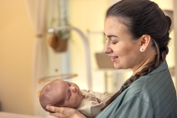 Mother gently cradling her newborn baby in soft warm light – infant feeding and breastfeeding support