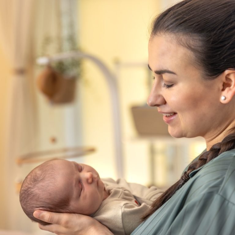 Mother gently cradling her newborn baby in soft warm light – infant feeding and breastfeeding support